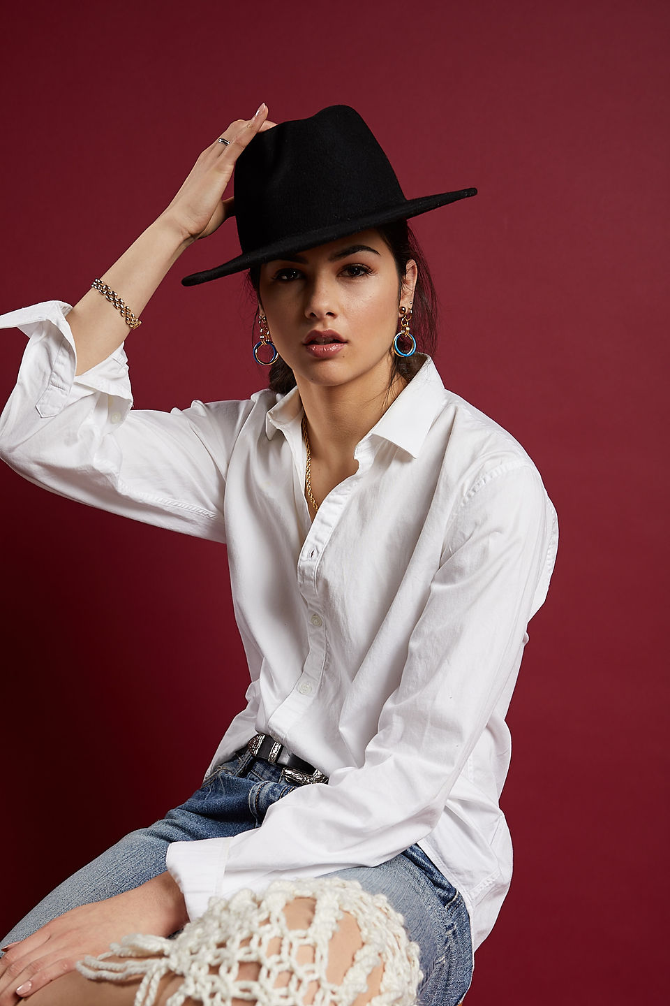 Female model sitting wearing a black felt fedora, white dress shirt, denim shorts with macrame insert and tan leather booties