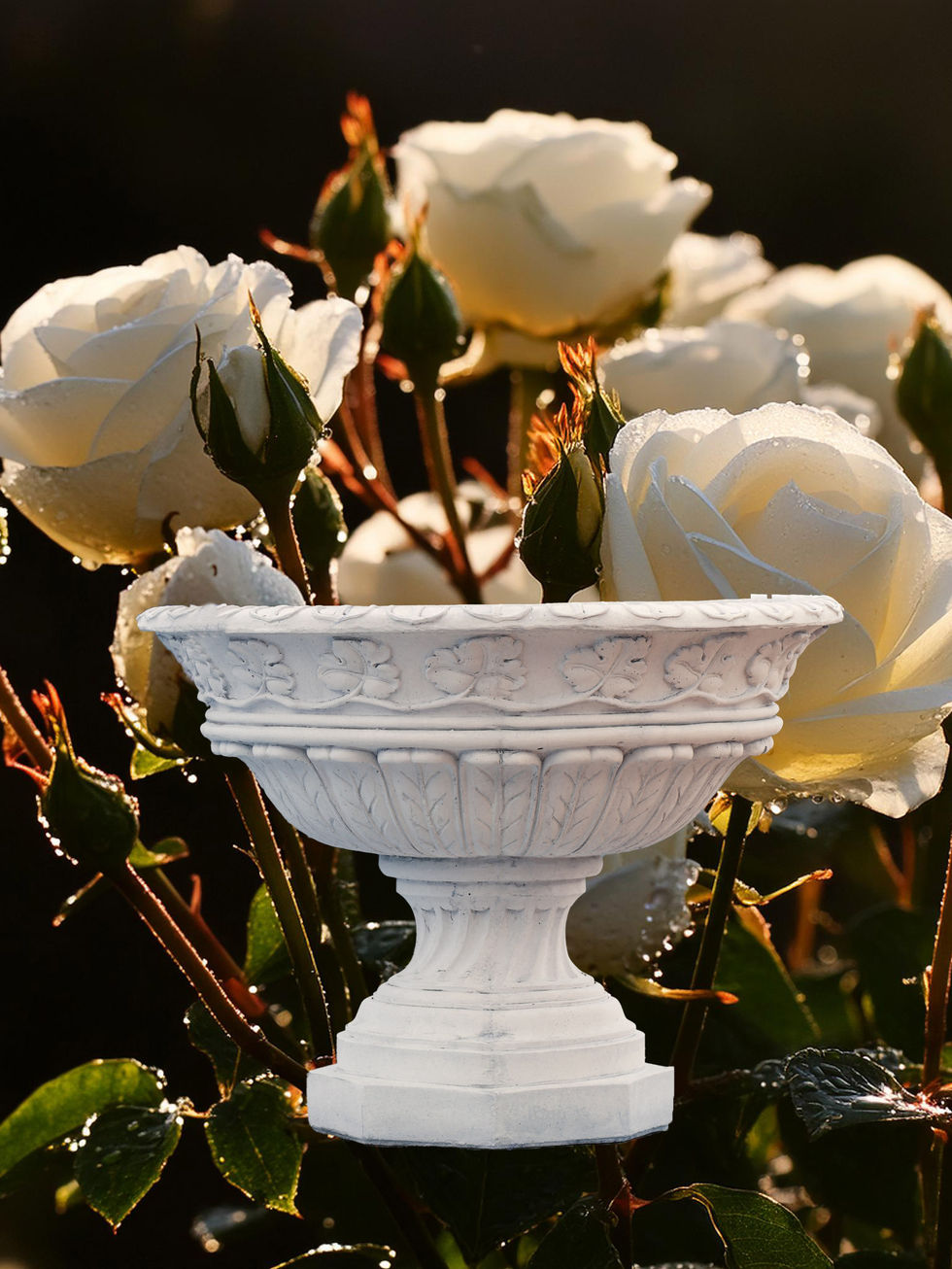 White urn planter with ornate details, surrounded by white roses in a garden setting