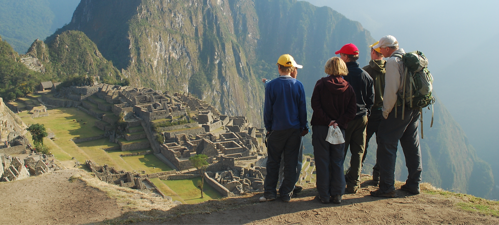 Four people with backpacks admire Machu Picchu ruins from a high vantage point, surrounded by misty mountains in the background.