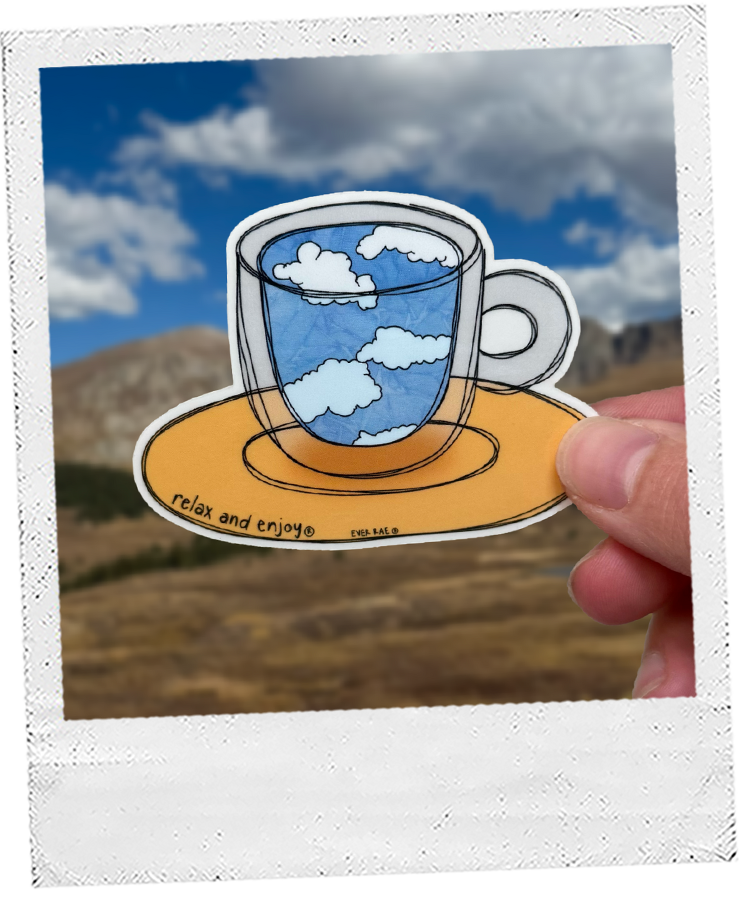 Thumbnail: hand holds a dreamy teacup sign sticker that says relax and enjoy with a bright blue sky and mountains in the background