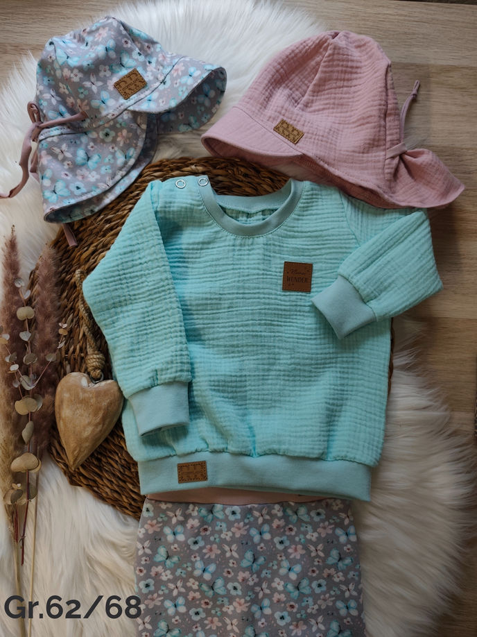 Kinderkleidung Set Gr.62/68: hellblauer Pullover, blumige Hose, zwei Hüte auf Fell.
