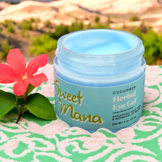 Sweet Mana's Cucumber Eye Gel on a beach towel next to pink flower