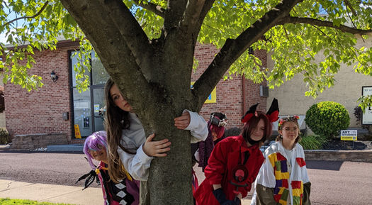 Summer camp kids in costumes they made themselves lined up behind a tree.