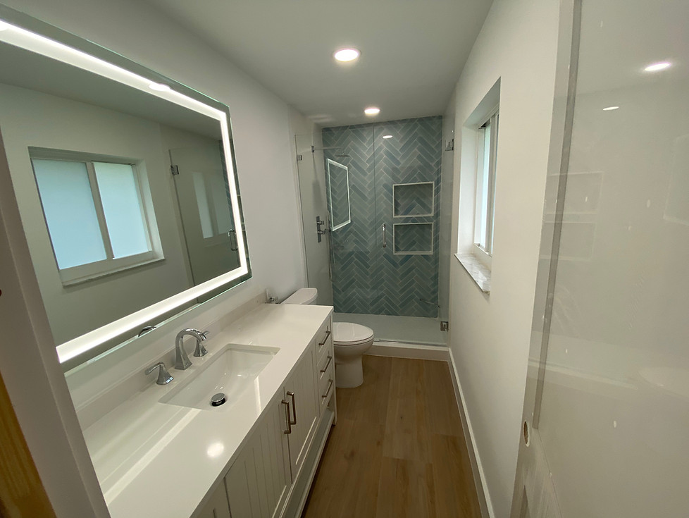 Modern bathroom remodel with white vanity and blue tile and LED mirror.