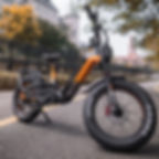 จักรยานไฟฟ้า fat‑tire (e‑bike) สีส้ม‑ดำ จอดบนทางป่าฤดูใบไม้ร่วง เหมาะกับทุกภูมิประเทศ