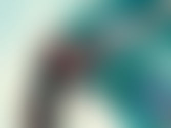 Woman in a white dress leans over a turquoise railing, gazing down with long hair blowing. Sky is overcast, creating a serene mood.