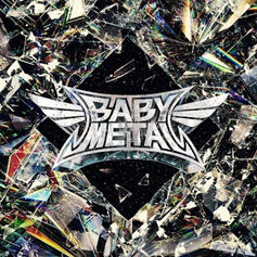 Silver "BABYMETAL" logo on a diamond shape, set against a colorful, fractal-like shattered glass background, creating a dynamic vibe.
