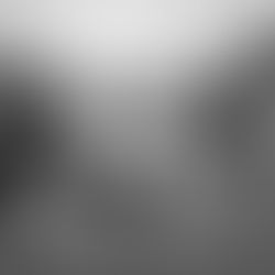 Person in beanie sitting on cracked pavement, head down, with two blurred figures moving past. Birds fly above; trees in background.