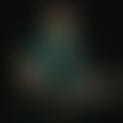 Bearded singer with glasses plays acoustic guitar and sings into a mic on a dark stage, focused and intimate.