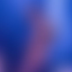 Singer performing energetically on stage with tattoos and bold makeup, blue-purple lighting, and a keyboardist in the background.