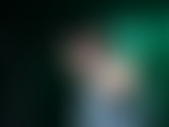 Singer in denim vest and cap performs energetically on stage under green lights, smiling into a microphone. Concert setting.