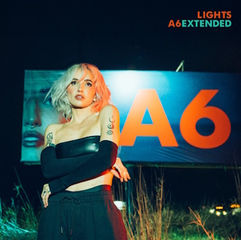 Woman with blonde hair stands in front of a bright "A6" billboard at night. She's wearing black with tattoos visible, mood is edgy.