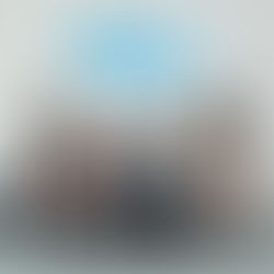 Six women sit on a brown sofa against a white wall with graffiti text "Sweet Tang." They wear stylish outfits and boots, exuding a confident vibe.