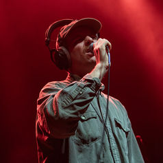 Singer wearing headphones and green shirt performs under red stage lights, holding a microphone with an intense expression.