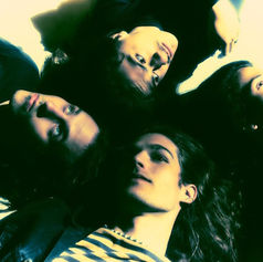 The four members of alt-grunge band Return to Dust lying on the ground, heads together in a circle, looking upward. The image has a greenish-yellow tint with a relaxed mood.