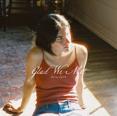 A woman, Avery Lynch, in a red tank top sits on a sunlit wooden floor. Text reads "Glad We Met" and "Avery Lynch." A patterned rug is partially visible.