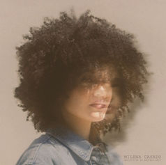 A person (Milena Casado) with curly hair in a blurred, dreamy effect, wearing a denim jacket. Background is neutral. Text reads "Milena Casado" and "Reflection of Another Self."