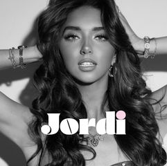 Woman poses with hands in hair, wearing bracelets, against a plain background. Black and white image with "Jordi" text. Glamorous mood.