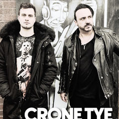 Two men in jackets stand in front of a mural with a figure. The mood is serious. Text reads "CRONE TYE." Brick and dark tones dominate.
