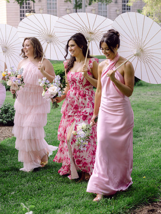 Bridesmaids walking with parasols in soft pink and floral dresses, highlighting romantic spring bridal fashion trends.