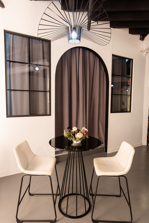 Modern bistro seating area with a round black table, white chairs, and an arched draped backdrop at our Chicago event venue.