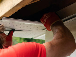 Accu-Dry technician in red work gloves installing aluminum gutters along a roofline, showing proper fascia attachment and gutter channel placement