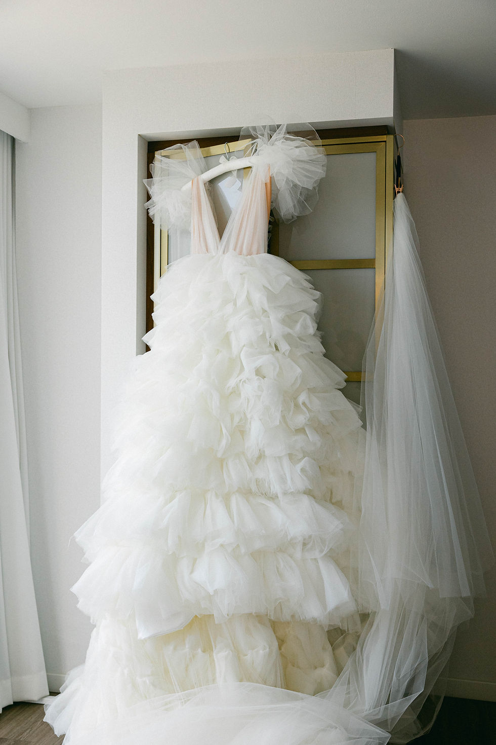 Bride’s voluminous ruffled tulle wedding gown hanging in a modern hotel suite, showcasing dramatic bridal fashion details.