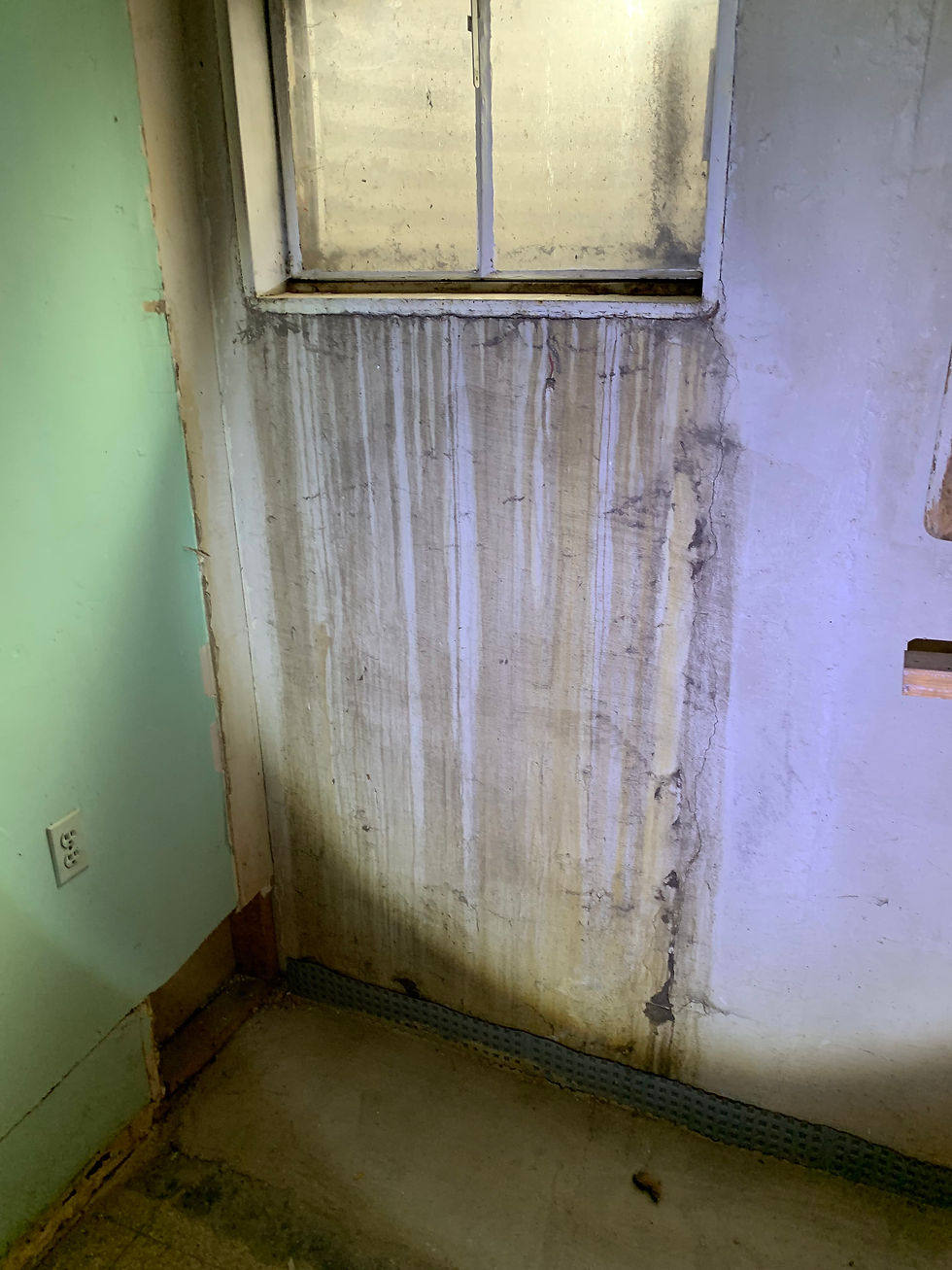 Severe water streaking and efflorescence on basement wall below window from sill plate seepage, with moisture damage extending to the floor