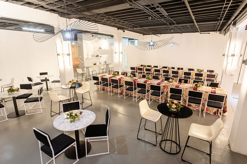Marble bistro tables and white stools in front of banquet rows at The Fulton West, a small West Town event venue in Chicago.