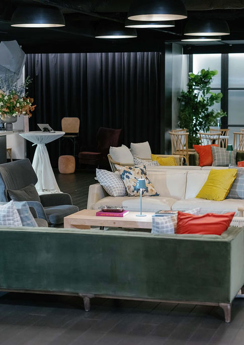 Lounge space at RPM Events on the Water in Chicago set up for a styled photo shoot, with photography lighting equipment visible near a lush floral arrangement, green velvet sofa, and mixed textured seating.