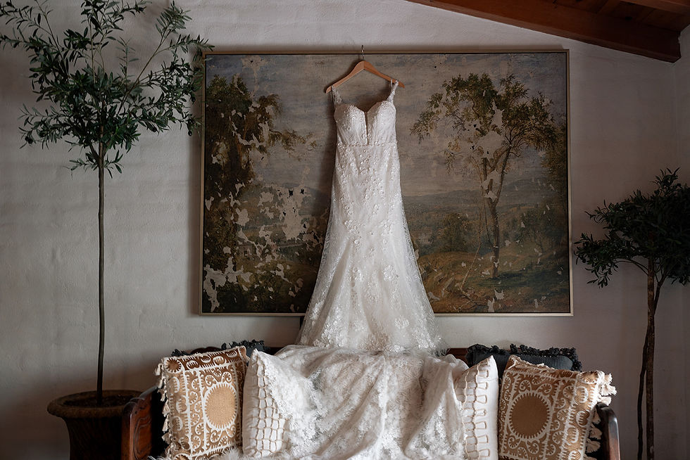 Martina Liana bridal gown draped over an antique wooden sofa inside Tivoli Italian Villa, with a distressed landscape oil painting on the wall behind it