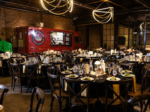 Wide view of a warehouse wedding venue with two food trucks and round tables set for dinner