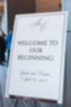 White sign with elegant script reads "Welcome to Our Beginning." Names "Jessica and Connor," date "April 26, 2025." Indoor event setting.