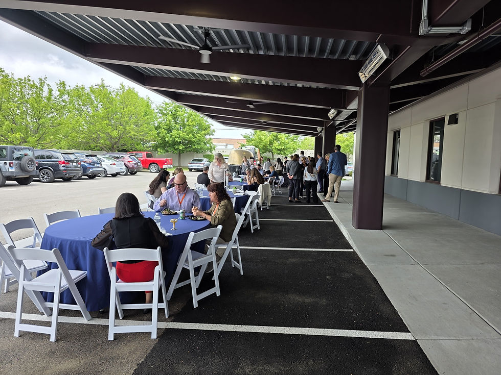 Guests dining at a corporate event catering setup with round tables and linens under a covered outdoor space