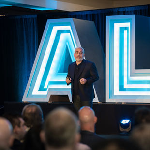 Presenter on the main stage in front of giant light-up ALL letters at Sysdig's 2023 sales kickoff at The Cosmopolitan in Las Vegas