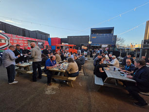 Corporate event attendees eating at picnic tables in front of multiple food trucks at an outdoor Chicago event