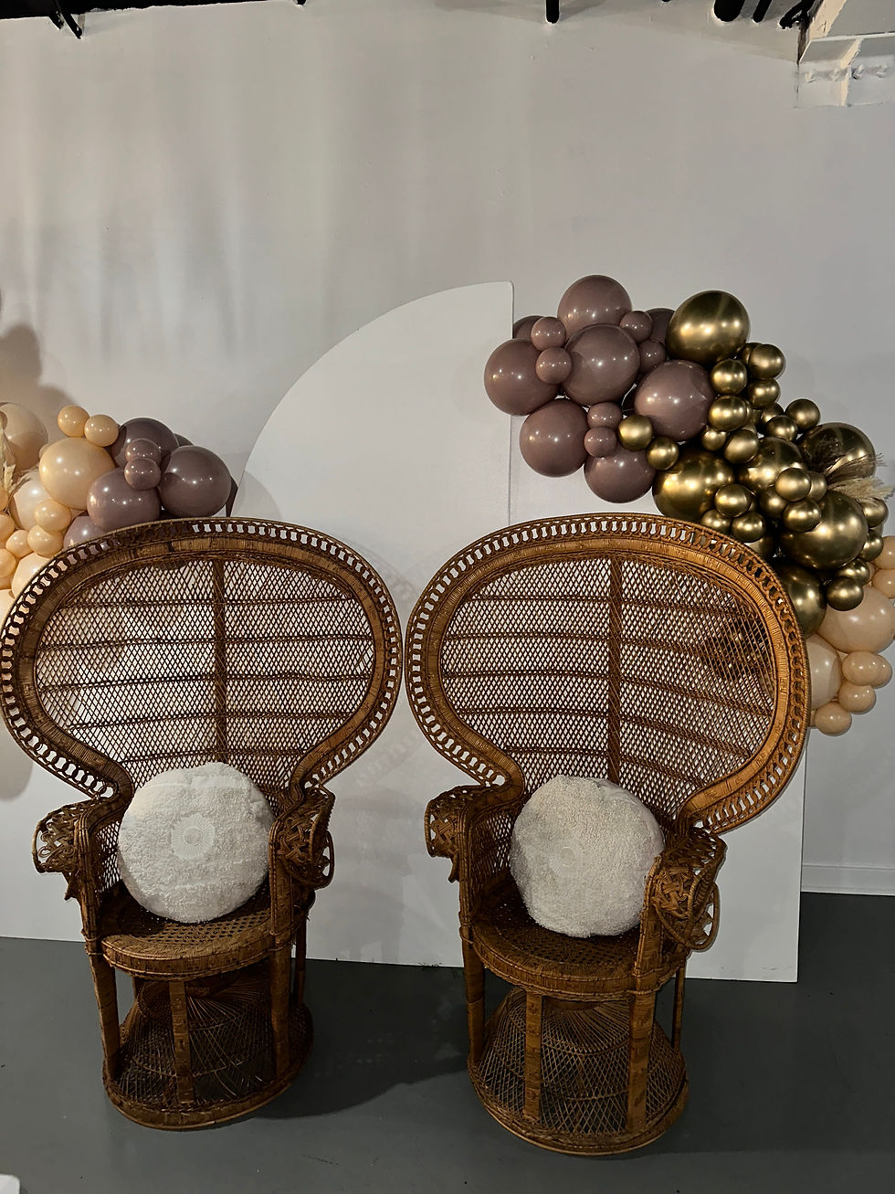 Two rattan peacock chairs under a mauve and gold balloon garland, set up as a photo spot at The Fulton West in Chicago