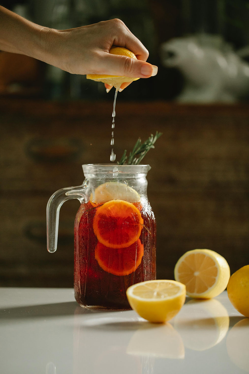 Jug of ice tea with lemon wedges and person squeezing more lemon juice into the jug