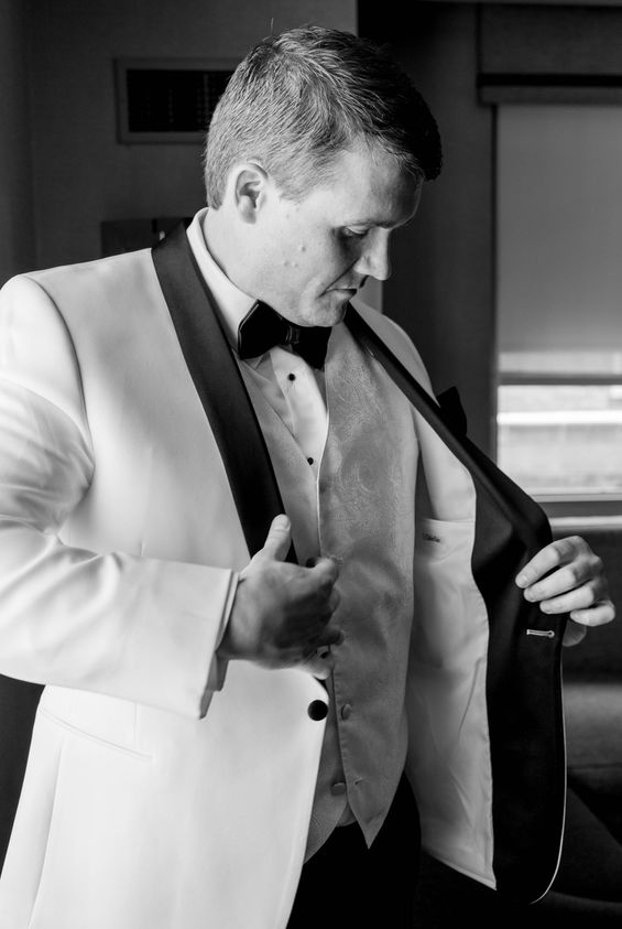 Black and white portrait of Michael adjusting his white dinner jacket over a vest and bow tie
