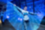 LED wings dancer poses with illuminated butterfly wings outside a nighttime event venue.