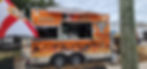 An orange food truck labeled "Yahuales Tacos" with Day of the Dead skull artwork and flames is parked behind a chain-link fence, with a Florida flag in the foreground.