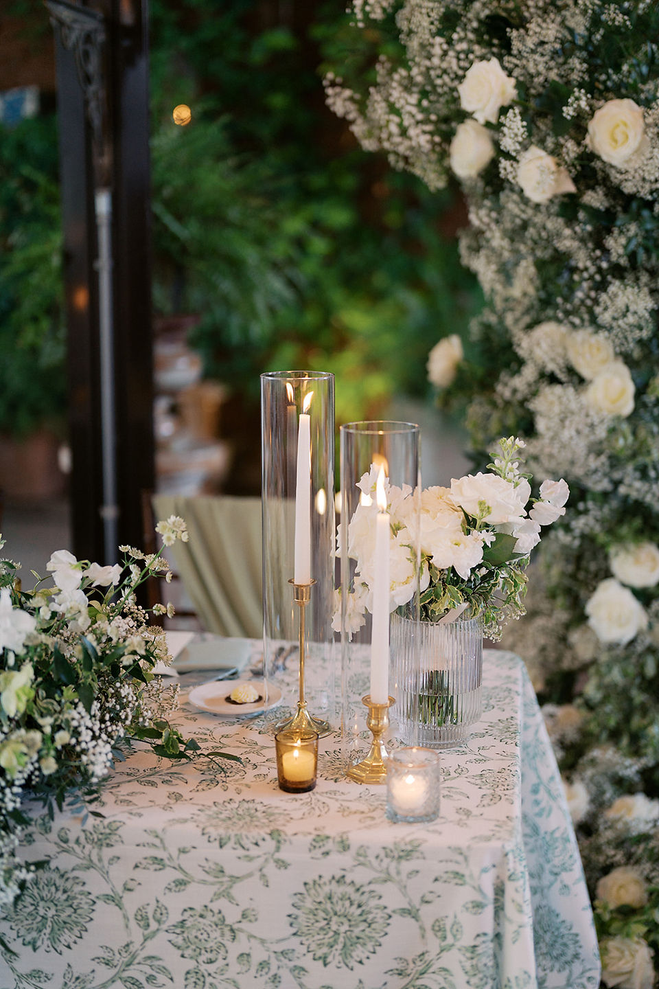Detail of sweetheart table at Galleria Marchetti with green patterned linen, white florals and tall candles.