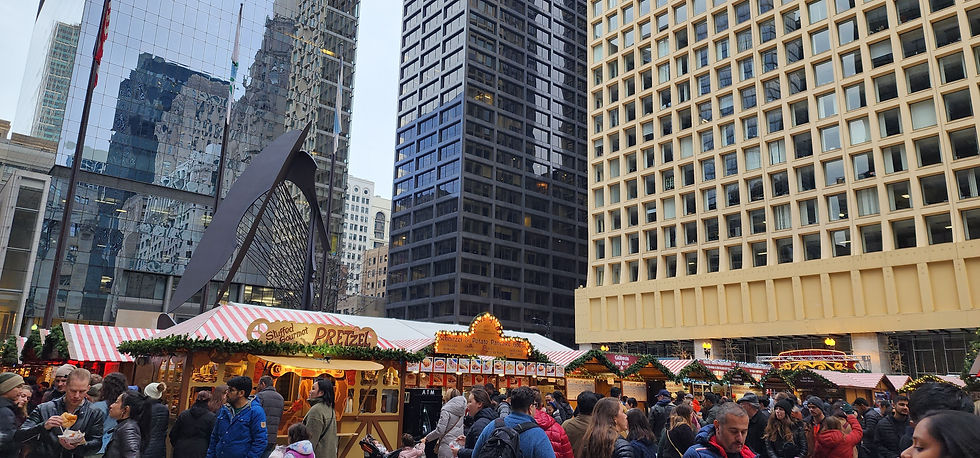 Crowd at an outdoor market with red-and-white tents beneath tall buildings. A man eats food, and signs read Pretzel and Schnitzel.