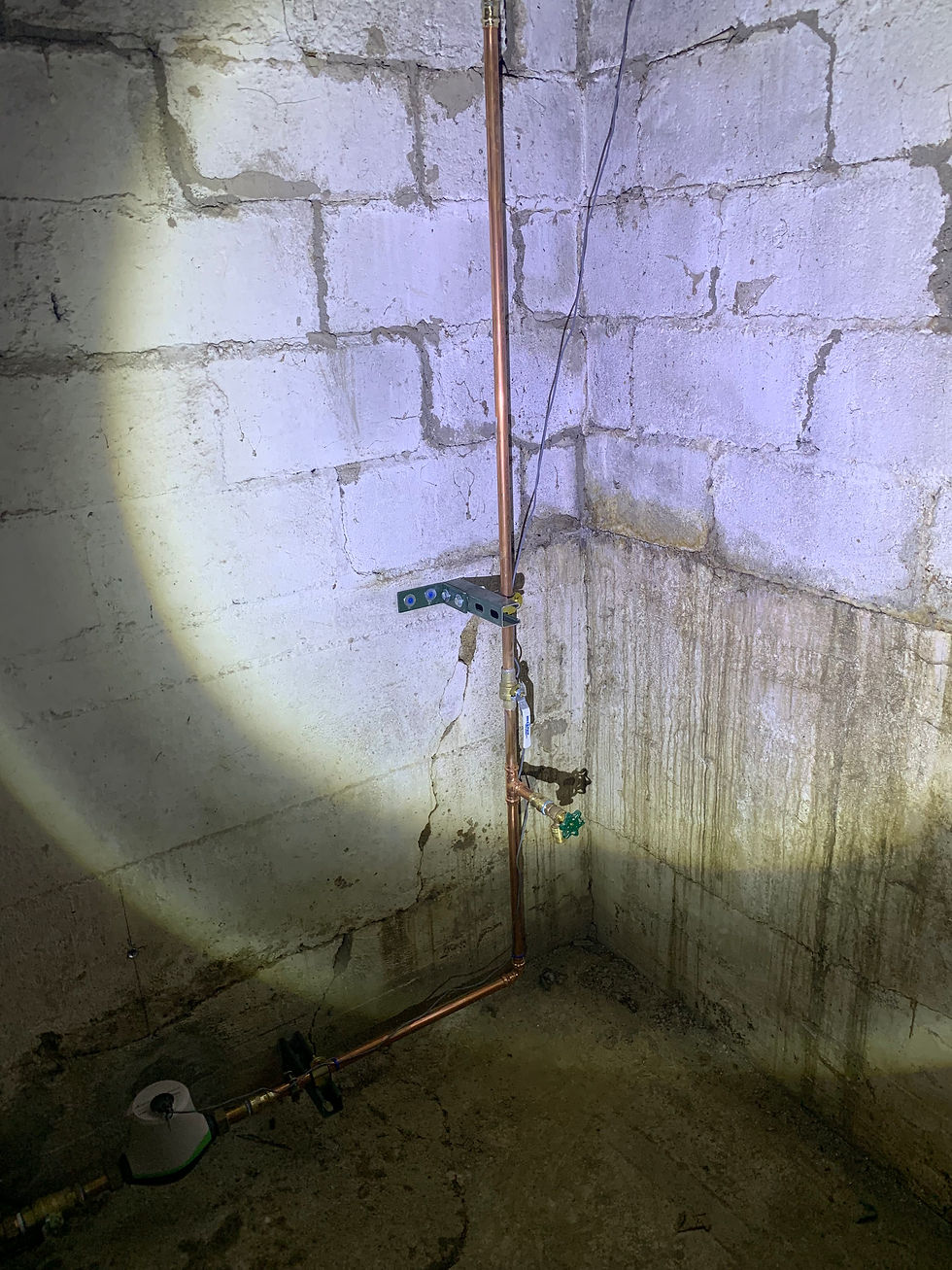 Cinder block basement wall corner with heavy white efflorescence and water staining streaking down the blocks alongside copper plumbing pipes