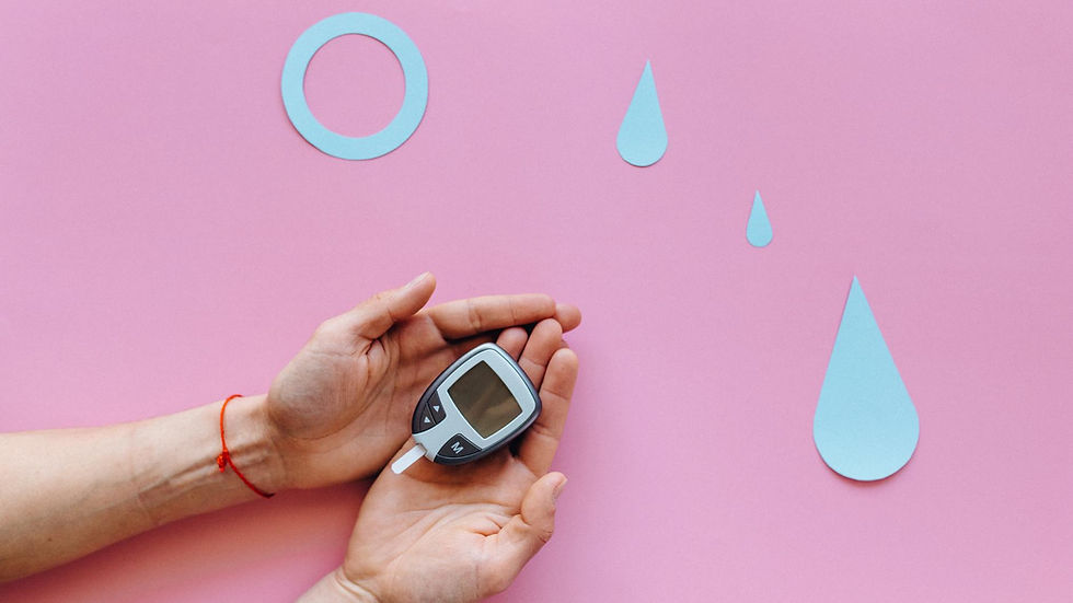 Hands holding a glucometer on a pink surface with blue diabetes symbols.