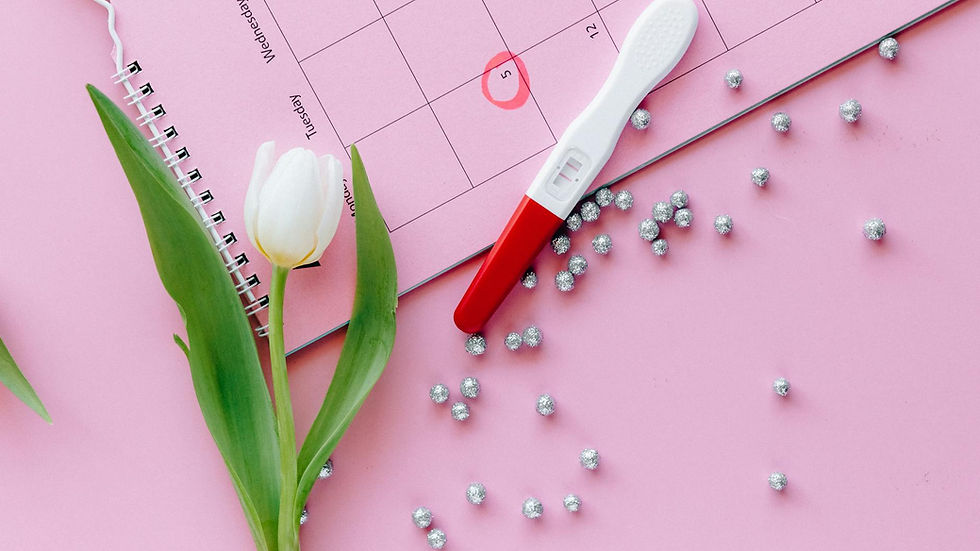 Calendar with a circled date, a pregnancy test, a white tulip, and silver beads on a pink background, creating an anticipatory mood.