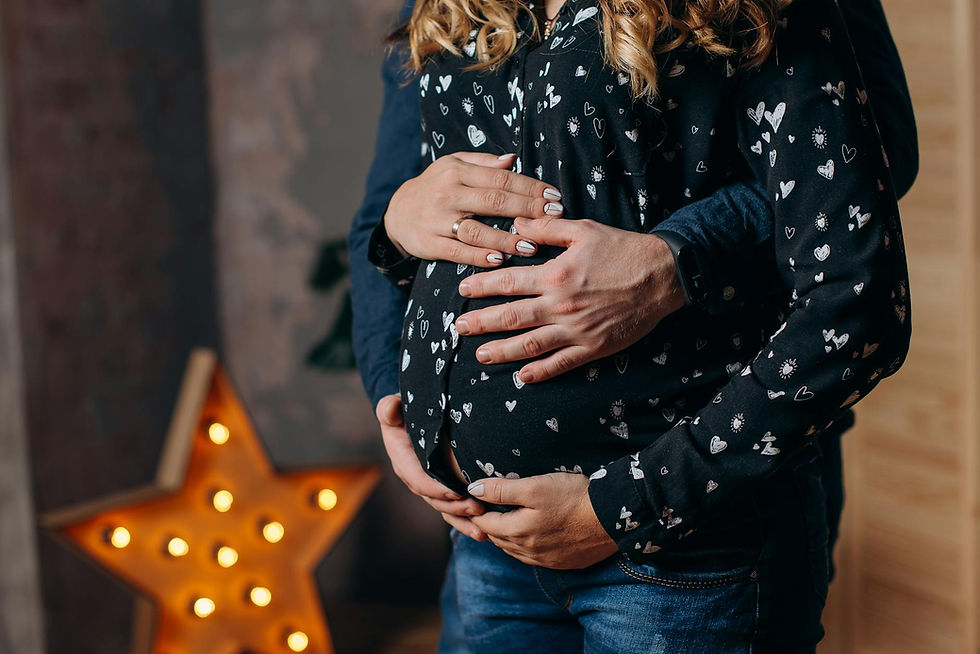 Hands gently holding a pregnant belly, wearing a black shirt with heart patterns. Warm lighting with a lit star in the background.