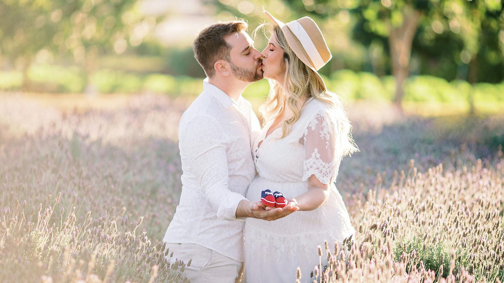 Expecting couple kissing in a lavender field, holding baby shoes with love and joy.