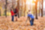 Child in blue takes a photo with a camera on a tripod of a pregnant woman and a boy in a park filled with autumn leaves and trees.
