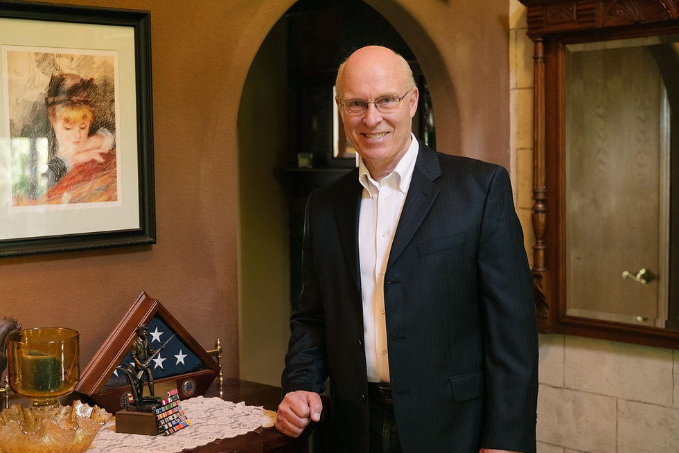 Mark Shull stands at home with his military decorations, American flag, and a bronze sculpture of military serviceman.